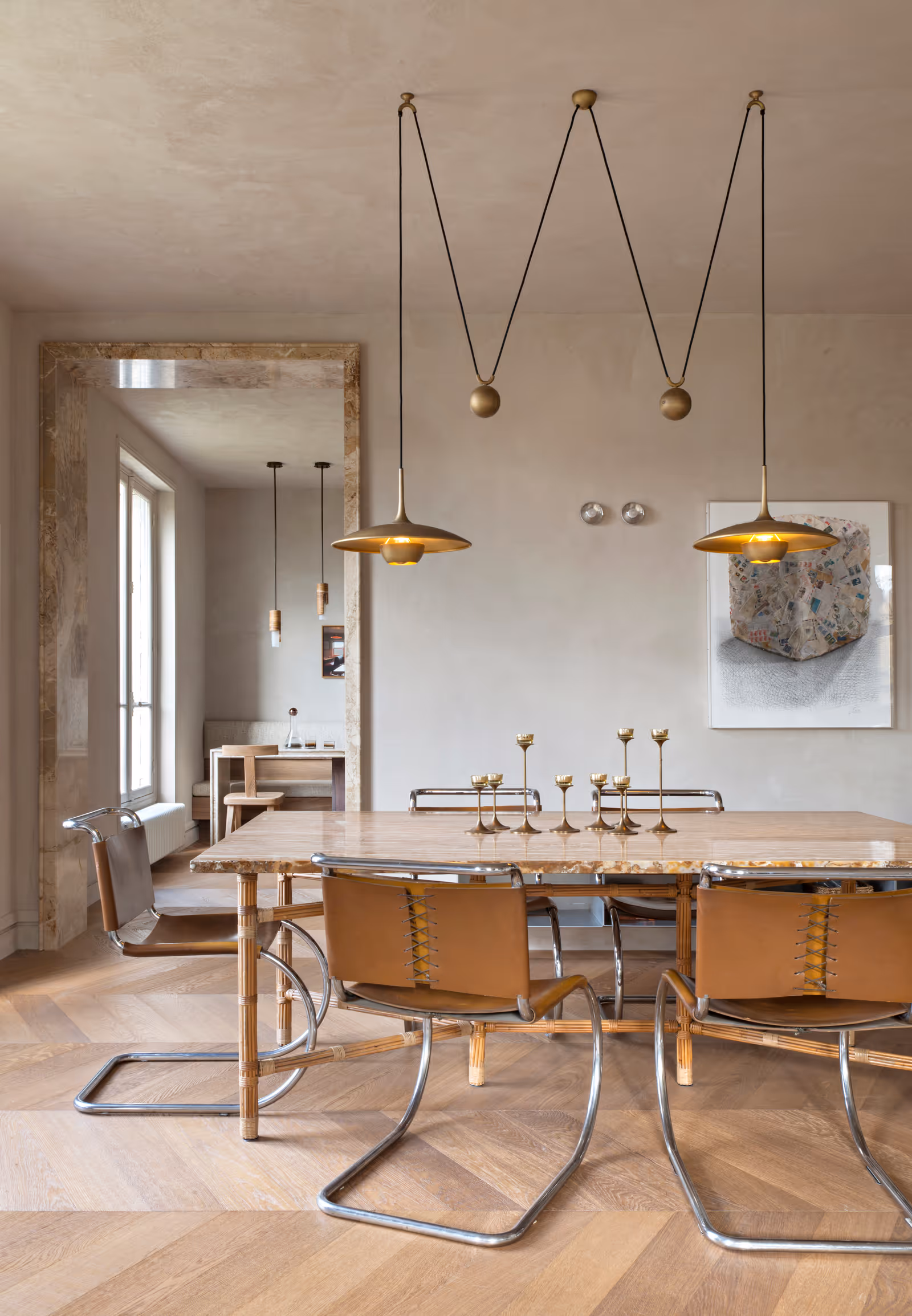 Salle à manger moderne avec une table en marbre, des chaises en cuir avec des structures métalliques, des bougeoirs en laiton et deux suspensions suspendues au plafond.
