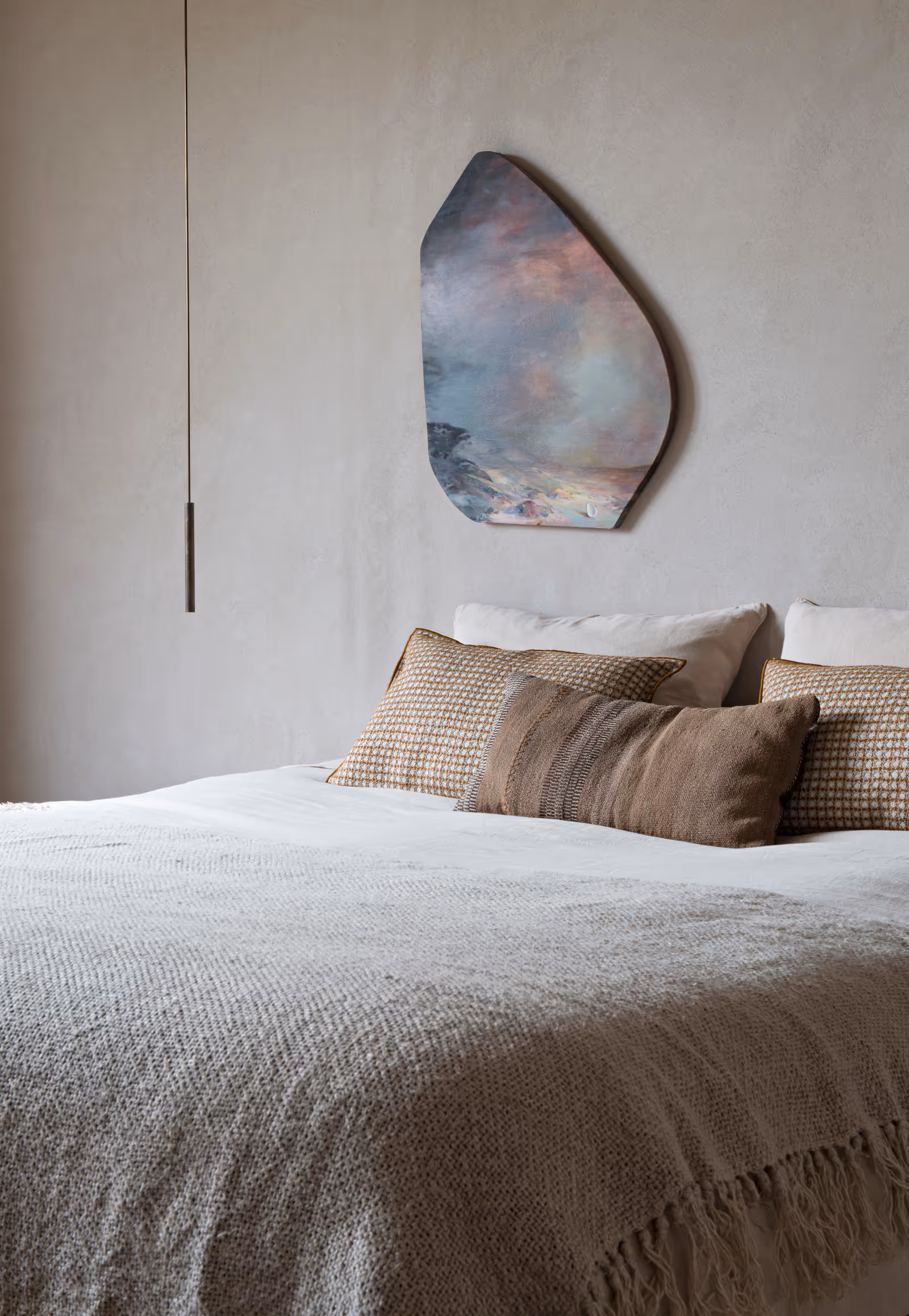 Lit avec couverture beige texturée, coussins assortis et décoration murale abstraite dans une chambre minimaliste.