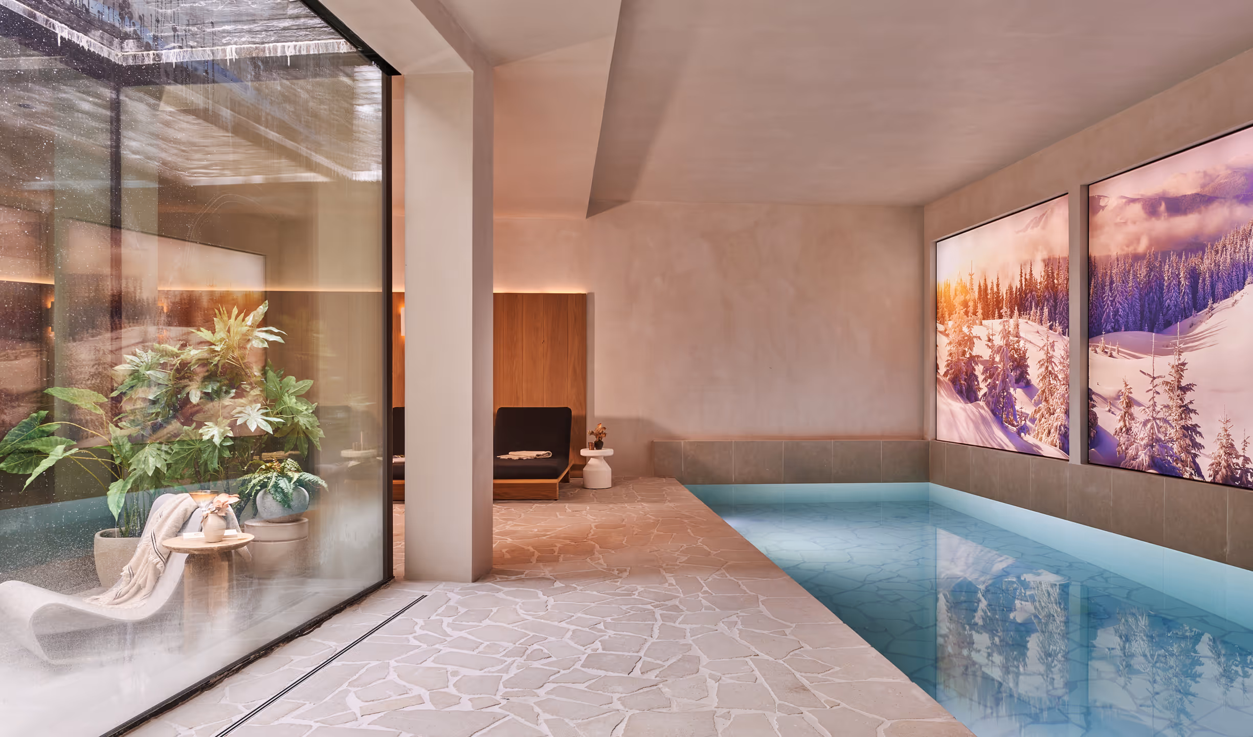 Piscine intérieure avec sol en pierre claire, chaises longues, plantes en pot et grands tableaux représentant des paysages montagneux enneigés accrochés aux murs.