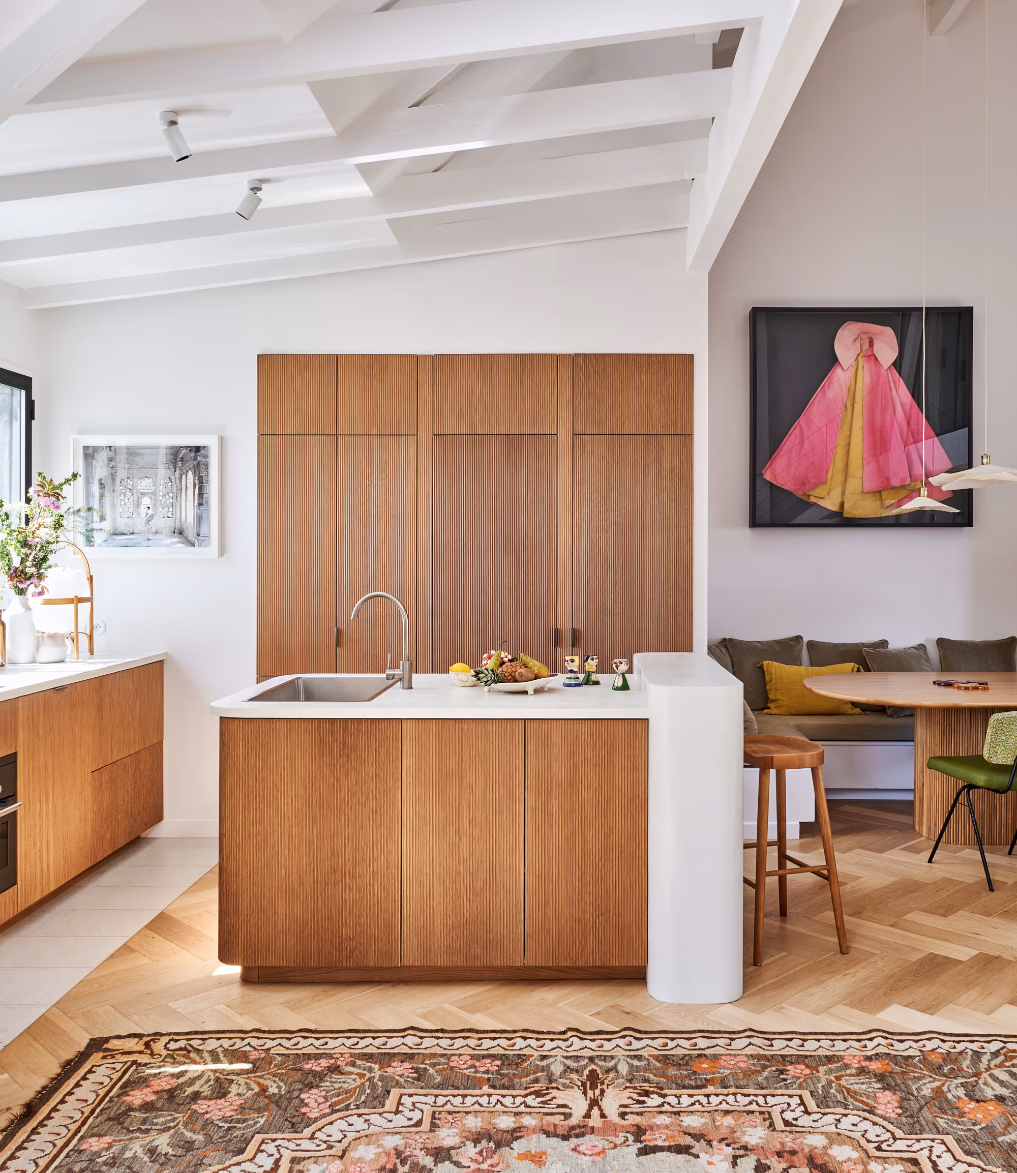 Cuisine moderne d'un duplex à Paris avec armoires en bois, comptoirs blancs, îlot central avec évier et coin repas avec sièges verts et marron et décorations murales colorées.
