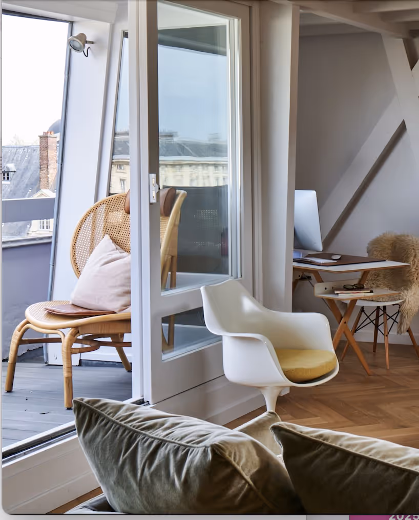 Espace de travail intérieur moderne avec fauteuil pivotant blanc et bureau d'ordinateur, à côté d'un balcon avec fauteuil en osier et coussin.