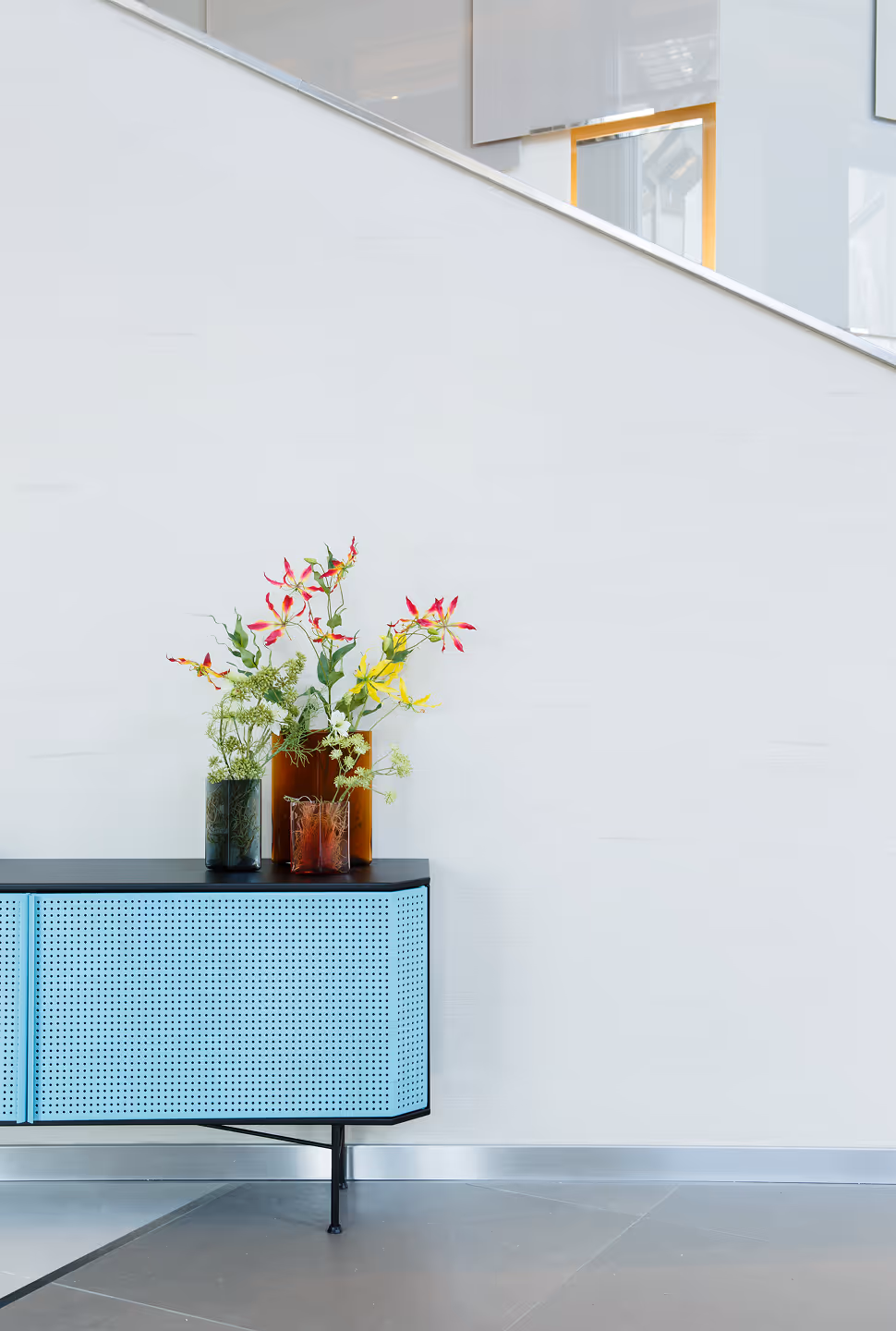 Buffet bleu moderne avec trois vases en verre contenant un assortiment de fleurs sauvages, posé contre un mur clair.