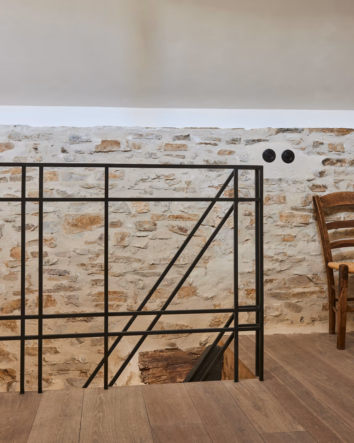 Parquet à côté d'une rampe métallique noire avec un mur en pierre et une chaise en bois dans un intérieur rustique.