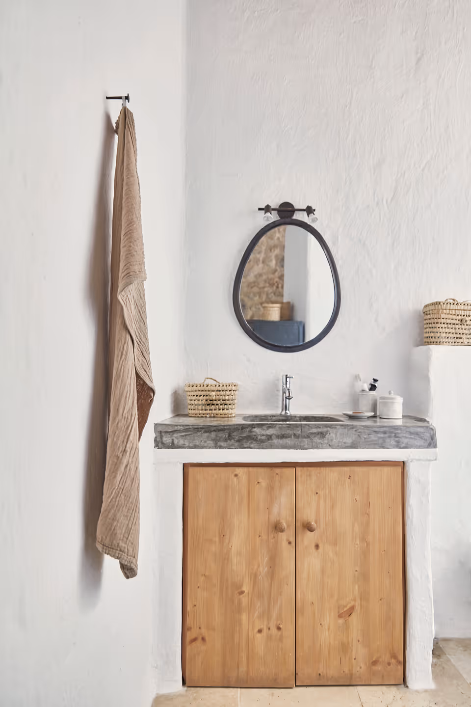 Lavabo minimaliste avec miroir rond à cadre noir, serviette beige accrochée au mur et meuble en bois en dessous.