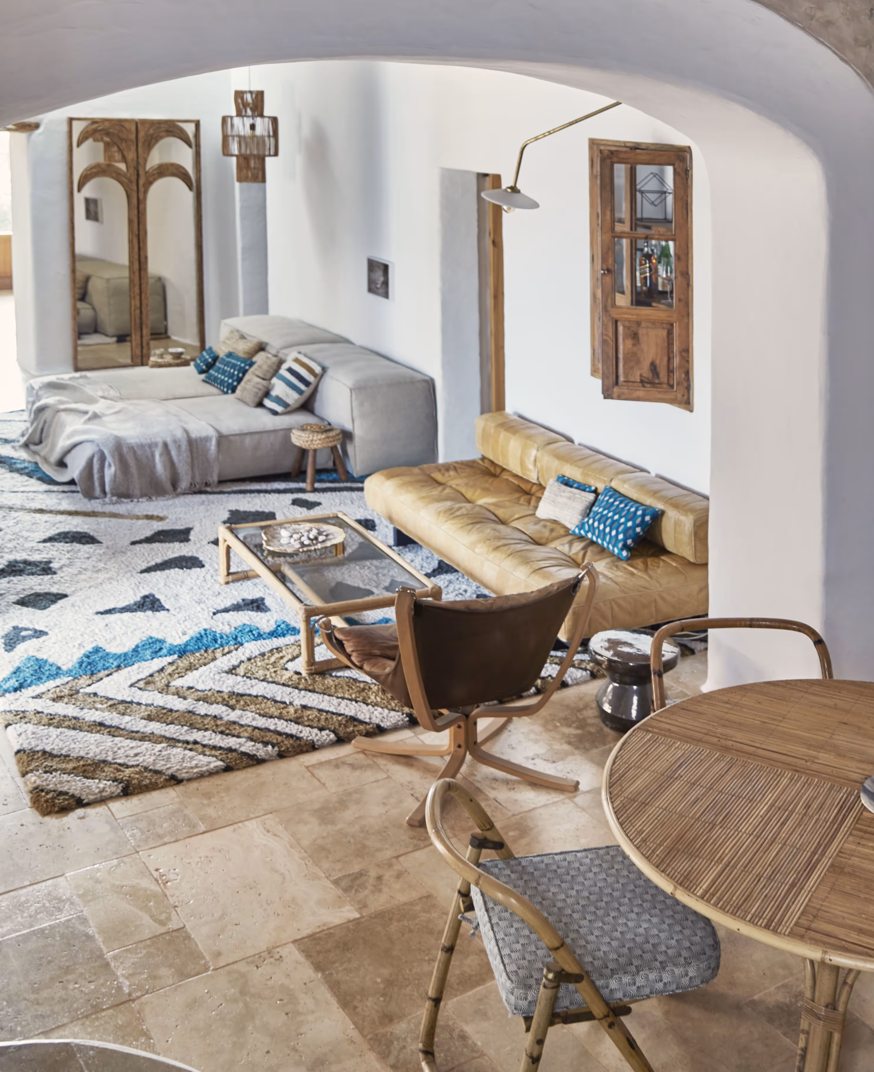 Salon confortable avec canapé en cuir beige, canapé d'angle gris, tapis à motifs, meubles en bois et murs blancs voûtés.